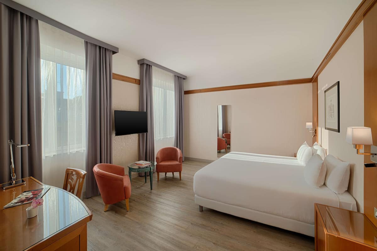 A hotel room with a bed, a desk, a chair, a TV, and a window with curtains.