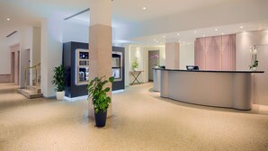 Una zona de recepción moderna con un mostrador curvo, plantas en macetas y una escalera que conduce a otro nivel.