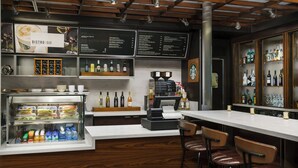 Una zona de bar con un mostrador refrigerado, estanterías con botellas y una pizarra de menú.