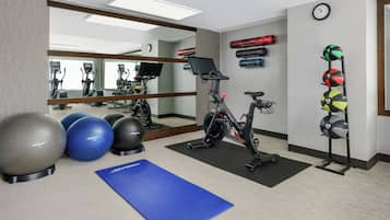 A gym with exercise equipment, a blue mat, and exercise balls.