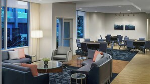 Un moderno vestíbulo de hotel con una zona de estar, una mesa de conferencias y grandes ventanales que ofrecen vistas a la ciudad.