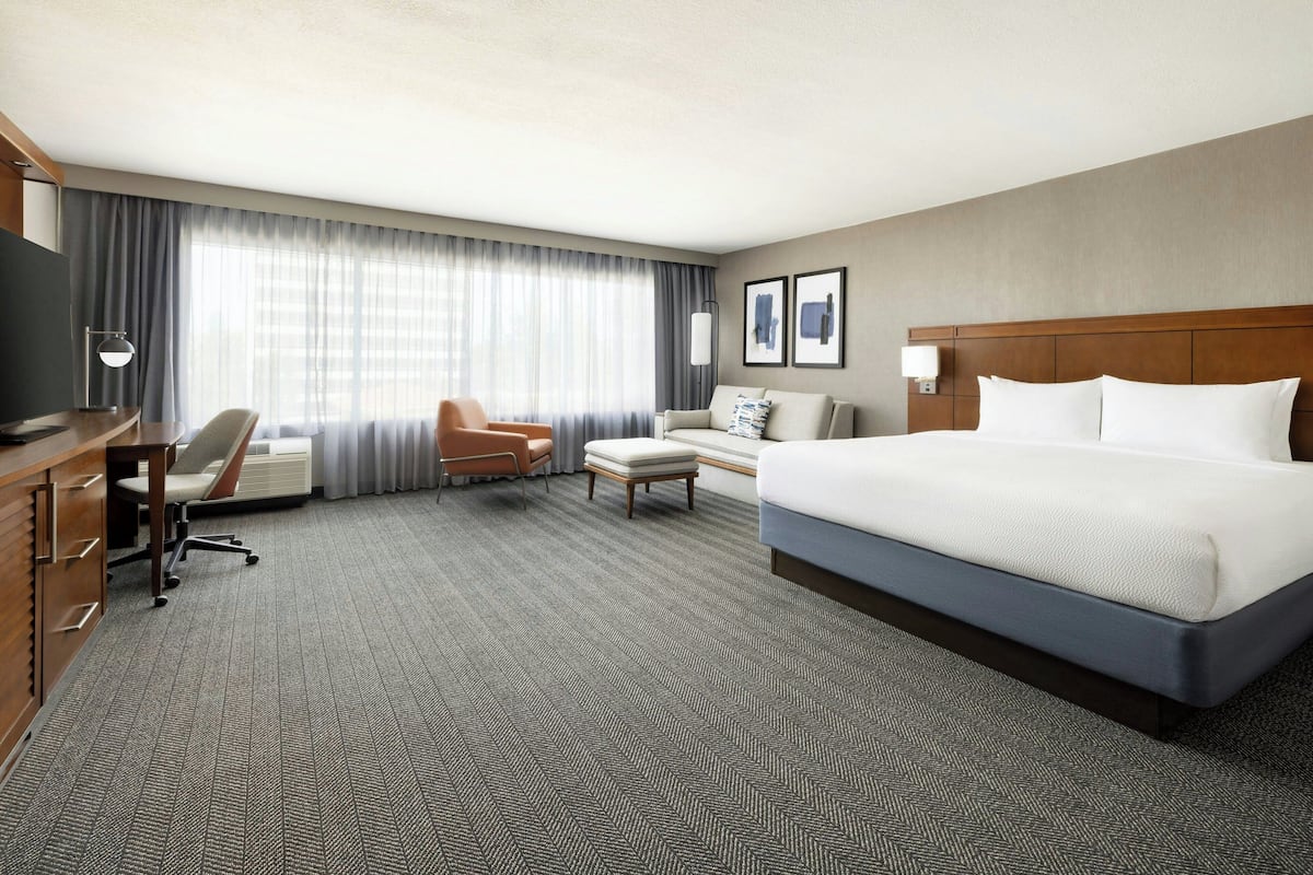 Ein Hotelzimmer mit einem großen Bett, einem Schreibtisch mit Stuhl, einer Couch und einem Fernseher.