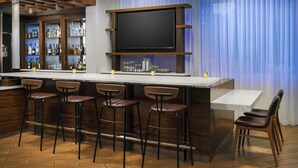 Zona de bar con televisor de pantalla plana grande, taburetes de madera y mostrador con botellas y vasos.