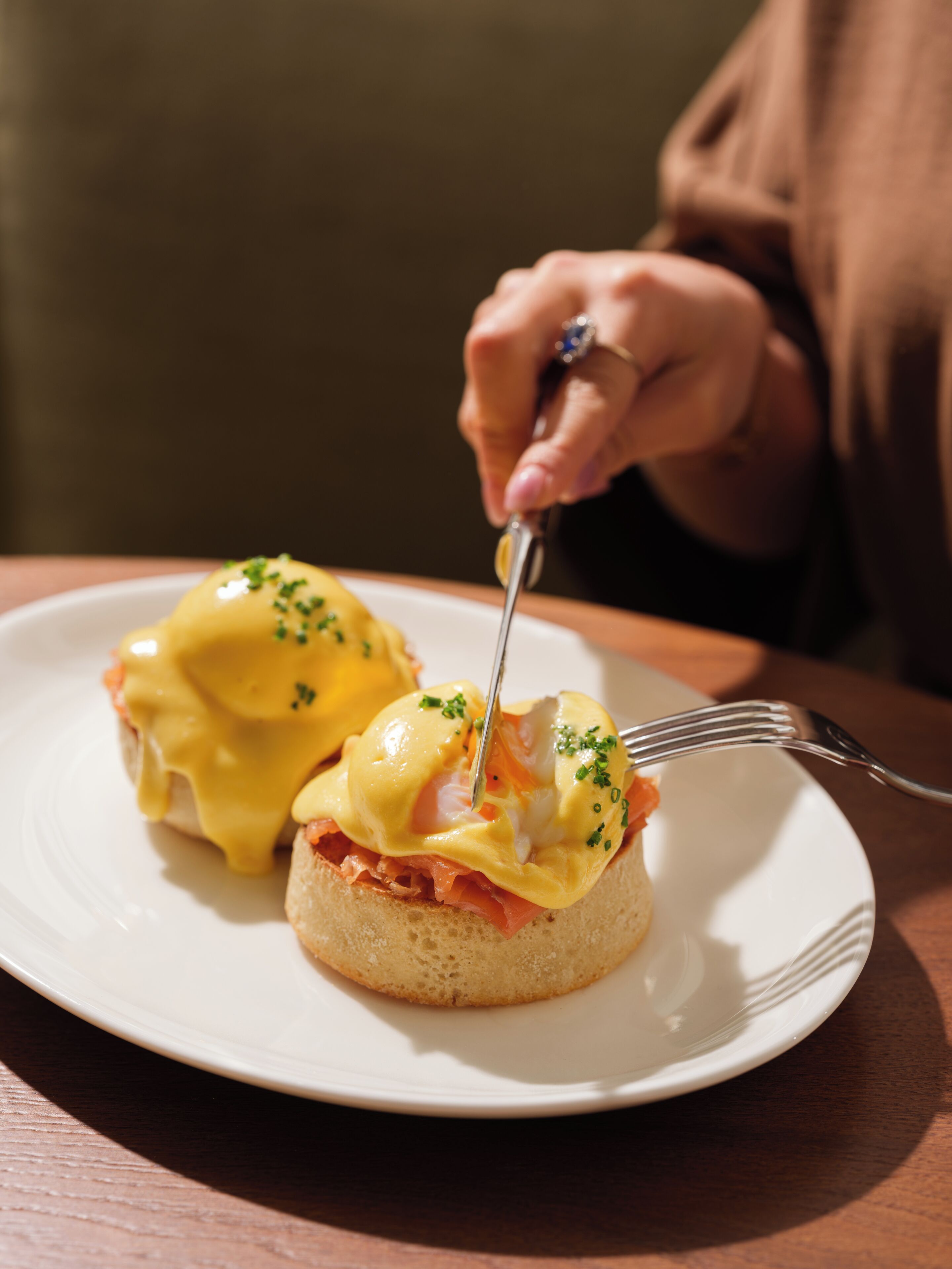 Ein Teller mit zwei Eggs Benedict, wobei eines gerade mit einer Gabel geschnitten wird.