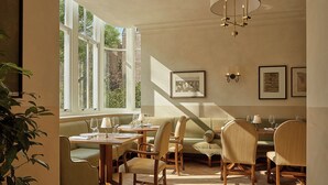 Un espace repas avec une table haute et des chaises, de grandes fenêtres et des œuvres d’art accrochées au mur.