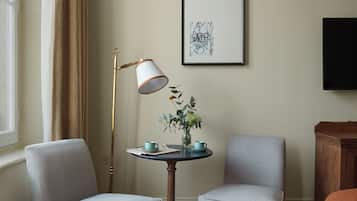 A room with two grey armchairs, a small round table with a vase of flowers, a floor lamp, and a framed abstract artwork on the wall.