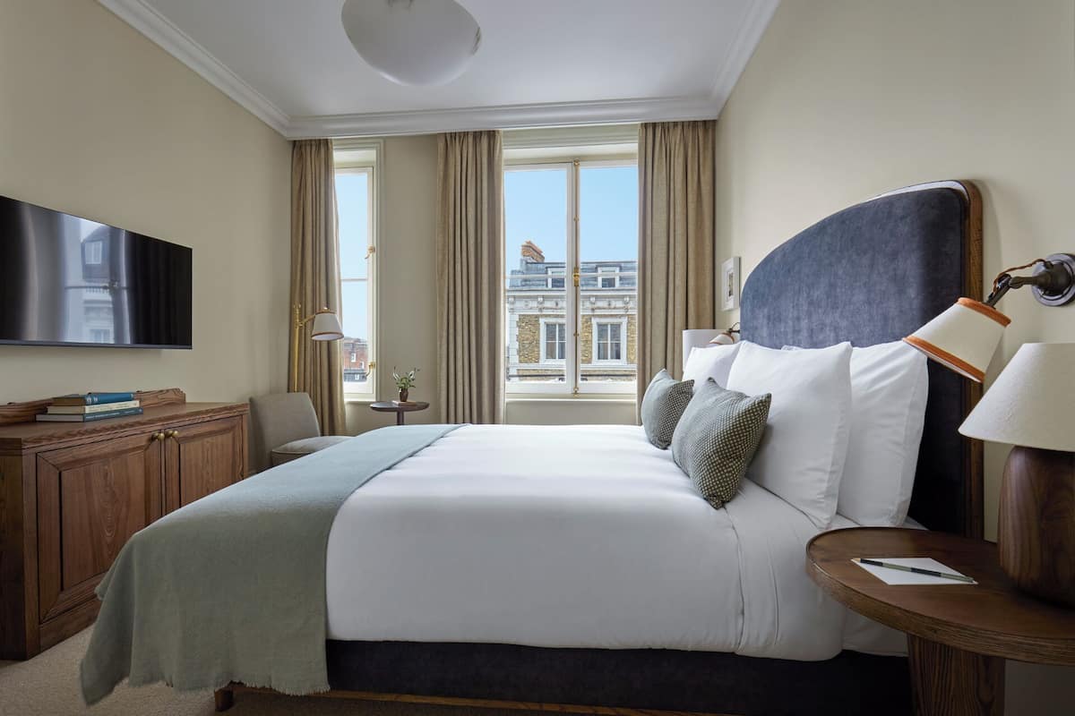 Ein Hotelzimmer mit einem großen Bett, einem Fernseher, einem Schreibtisch und Blick auf ein Gebäude.