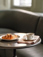 A table with a croissant and a cup of coffee on a tray, placed on a couch.