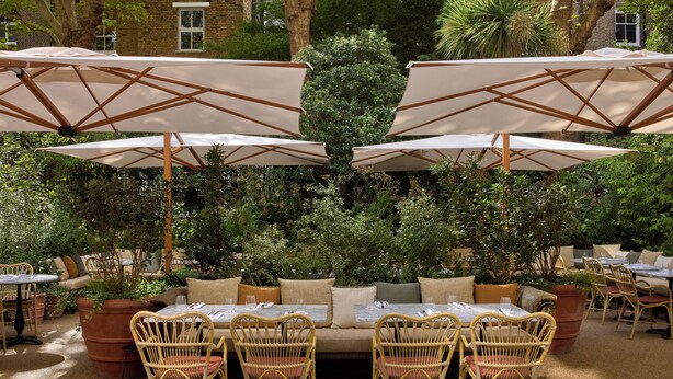 Un espace extérieur aménagé avec des tables et des chaises en osier, entouré de grands parasols et de plantes en pot.