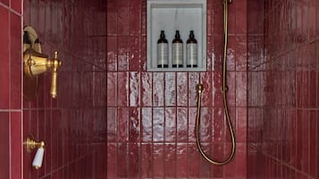 A bathroom with red tiled walls, a showerhead, and three bottles of shampoo in a white shelf.
