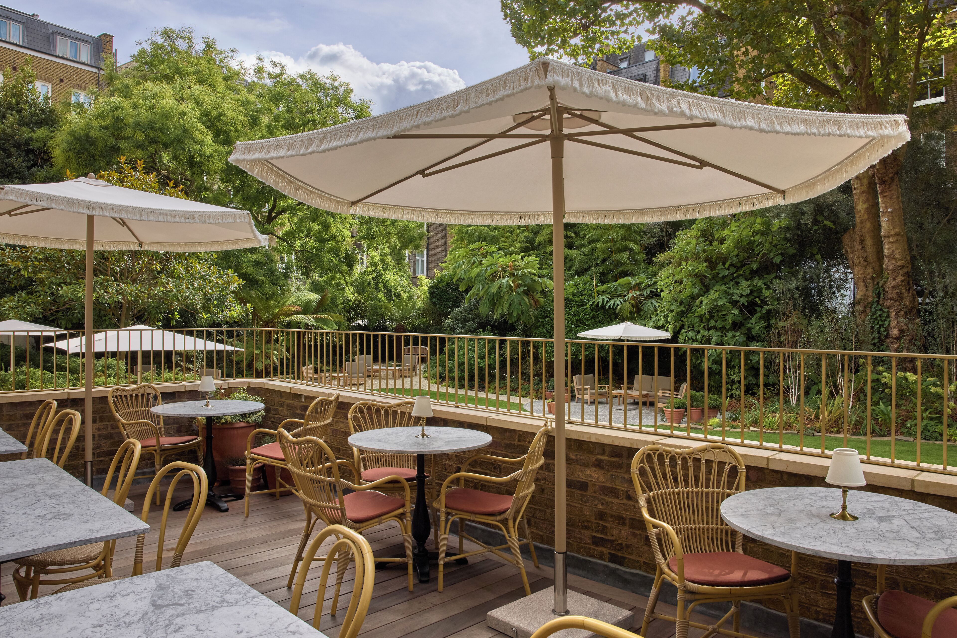 An outdoor patio with wicker chairs and tables, surrounded by a brick wall and greenery.