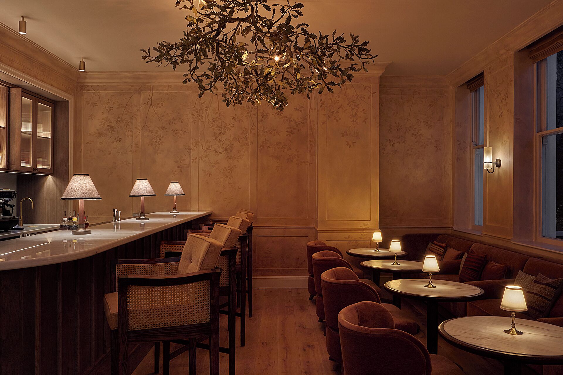 Zona de bar con poca luz, una barra de madera, varios taburetes y un candelabro.