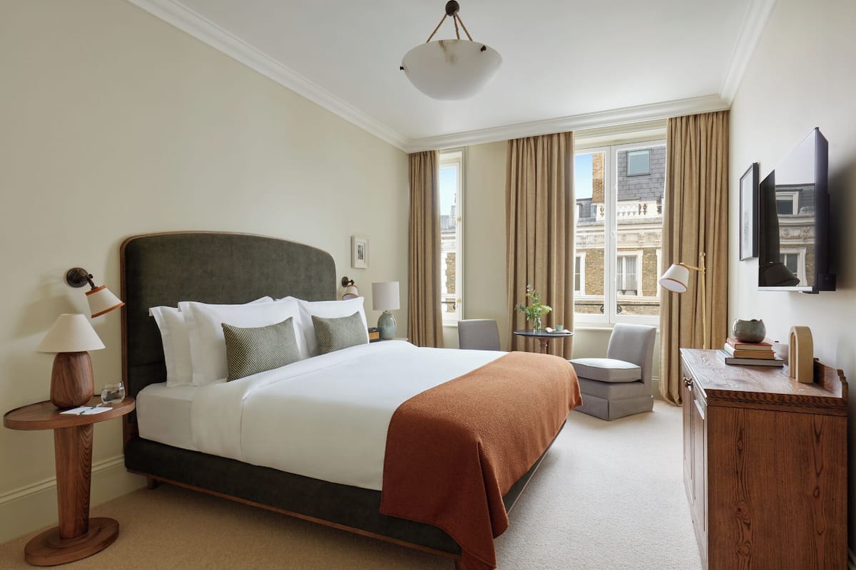 Ein Hotelzimmer mit einem großen Bett, einem Schreibtisch, einem Stuhl, einem Fernseher und einem Fenster mit Vorhängen.