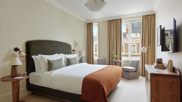 A hotel room with a large bed, a desk, a chair, a television, and a window with curtains.