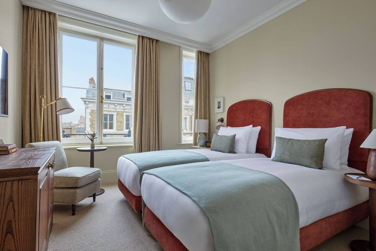 Ein Hotelzimmer mit zwei Betten, einem Schreibtisch und Blick auf Gebäude.