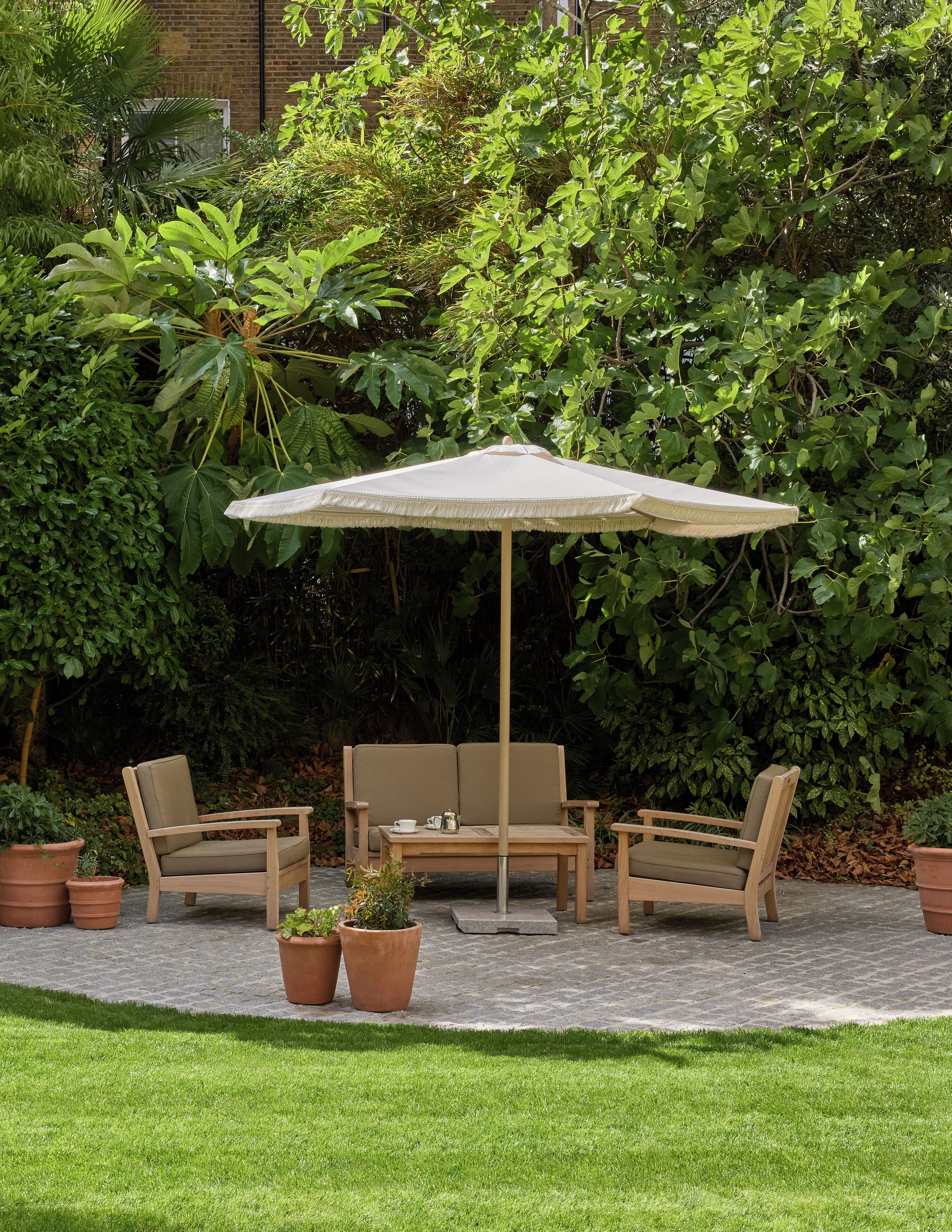 An outdoor seating area with a wooden bench and chairs, a table, and a large umbrella.