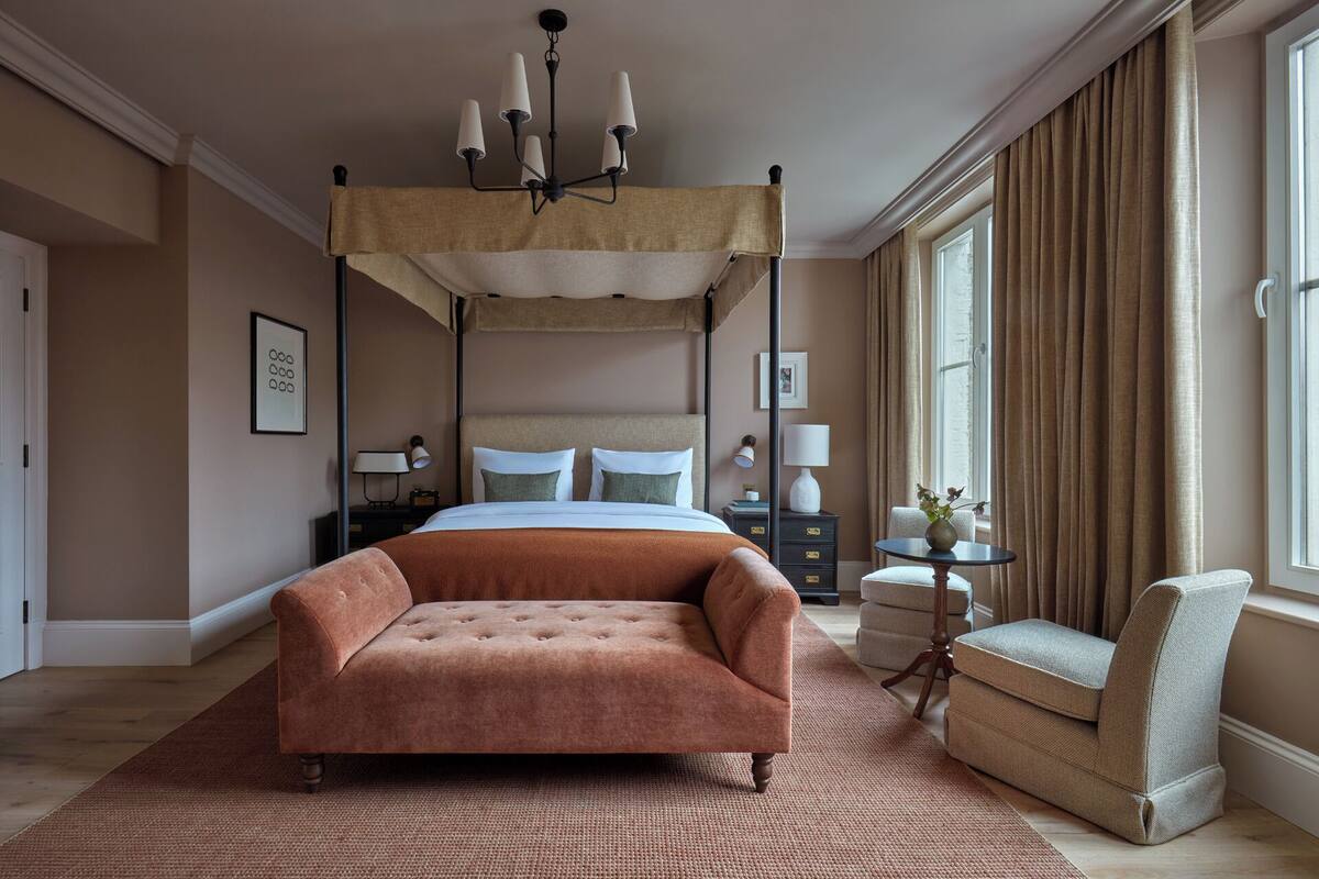 Ein Schlafzimmer mit einem Himmelbett, einer gepolsterten Couch, einem kleinen runden Tisch und einem Sessel.