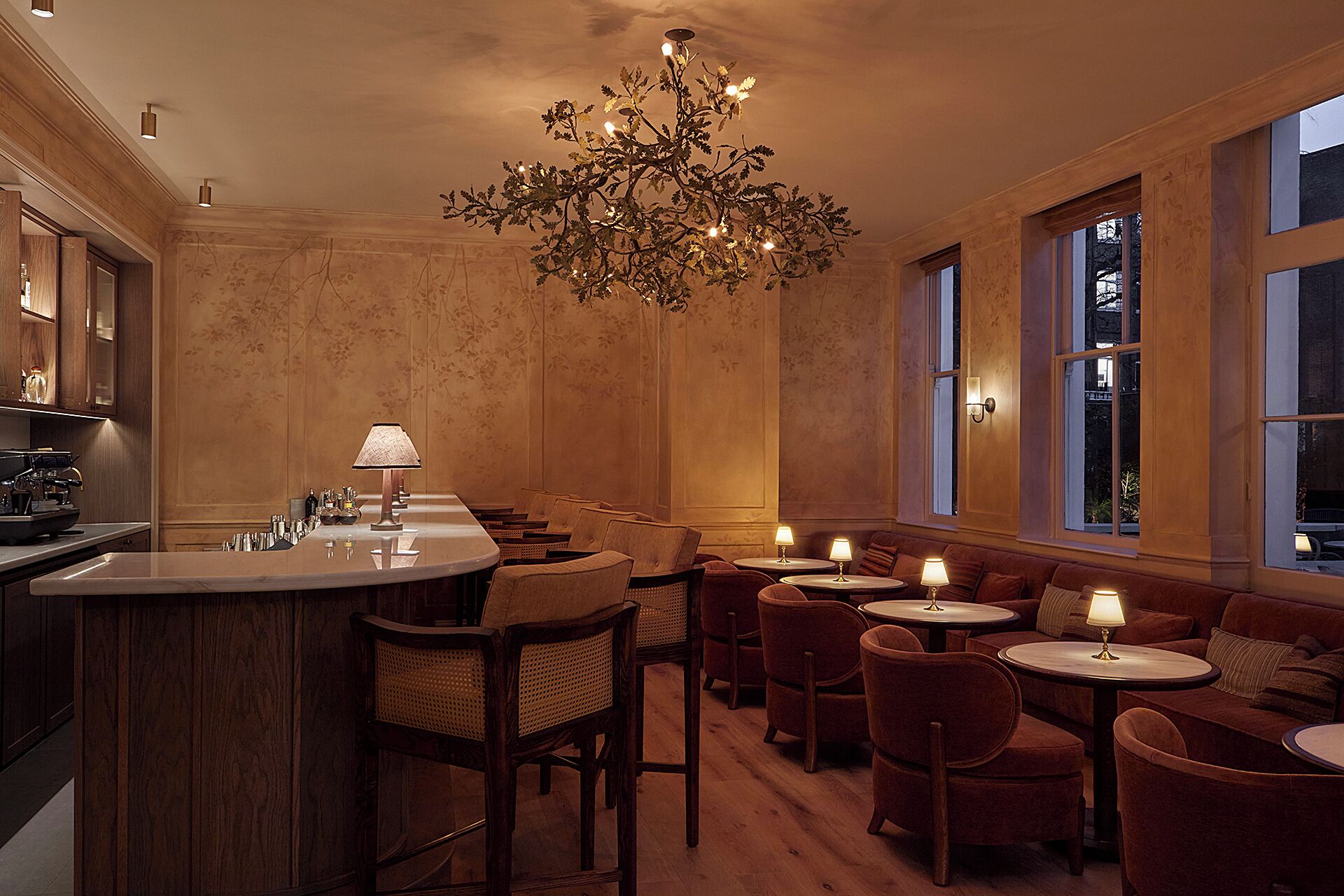 A bar area with a counter, chairs, and tables, and a chandelier.