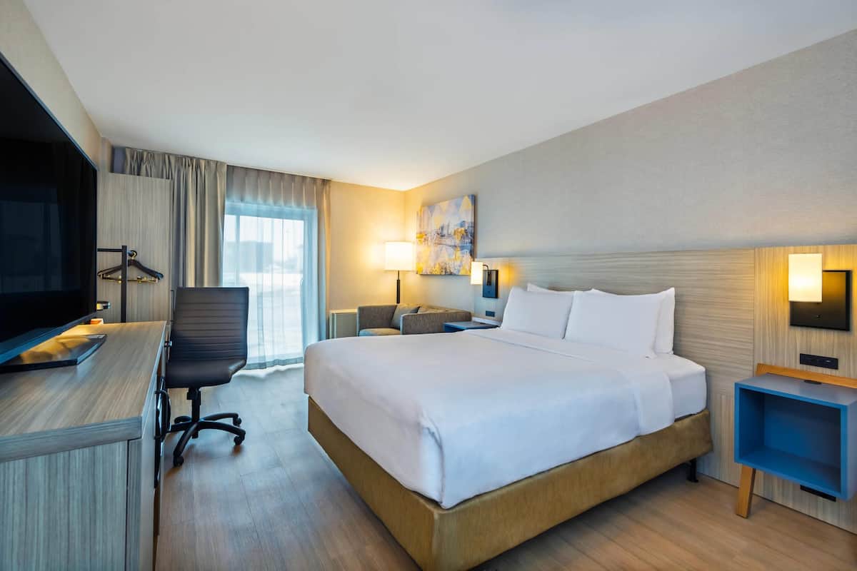 A hotel room with a bed, desk, chair, TV, and a painting on the wall.