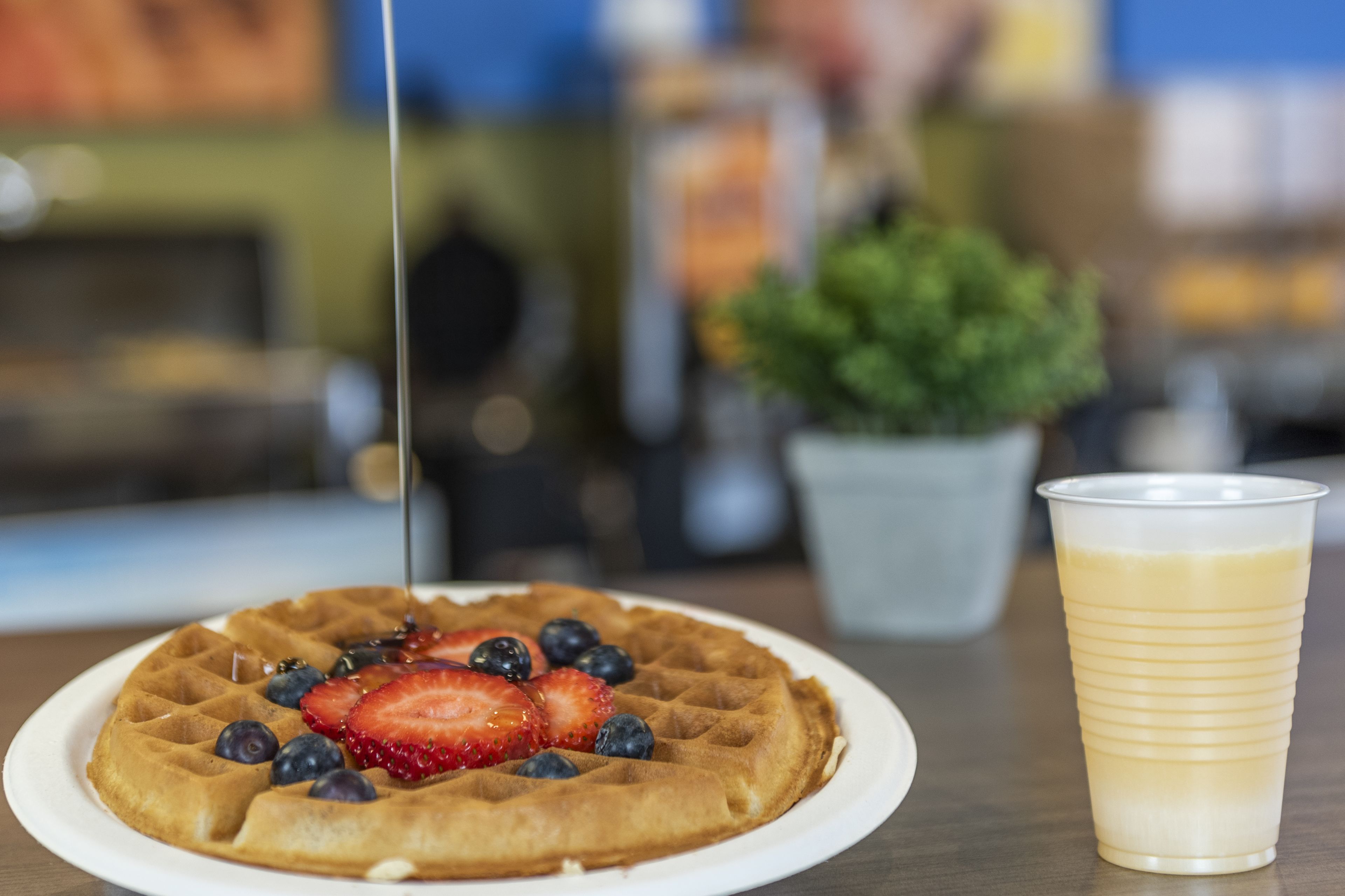 A waffle with fruit on a plate and a cup of coffee on a table.