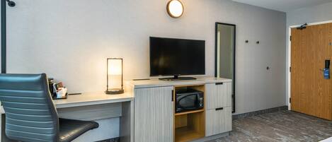 A hotel room with a desk, a chair, a flat-screen TV, a microwave, and a wooden door.