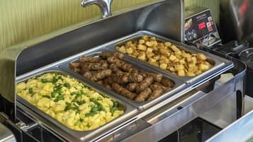 A buffet with three trays of food: scrambled eggs, sausages, and roasted potatoes.