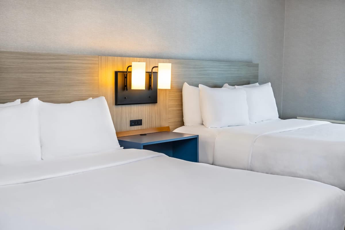A hotel room with two beds, a nightstand, and a wall-mounted light fixture.