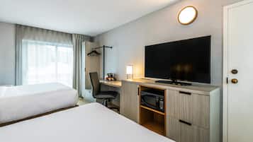 A hotel room with two beds, a desk with a TV, a coffee machine, and a wardrobe.