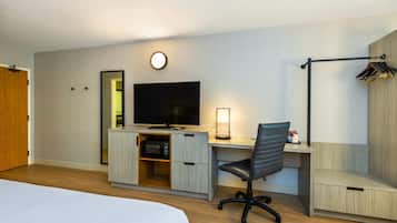 A hotel room with a bed, a desk with a computer, a TV, a mirror, and a coat rack.