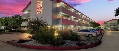 Um hotel com letreiro de neon, vários andares e estacionamento.
