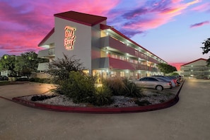 Un hotel con un letrero de neón, varios pisos y un estacionamiento.