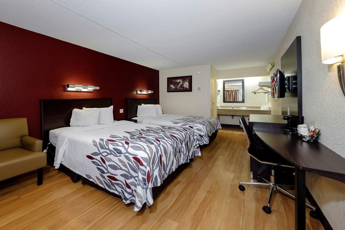 A hotel room with a bed, a desk, a chair, and a mirror.
