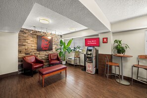 A Red Roof Inn lobby with leather chairs, a wooden bench, an ATM, and a sign indicating free Wi-Fi in all rooms. - Red Roof Inn Dallas - DFW Airport North (Irving)