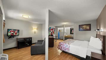 A hotel room with a bed, a desk, a television, and a seating area.