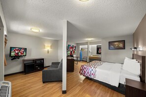 A hotel room with a bed, a desk, a television, and a seating area. - Red Roof Inn Dallas - DFW Airport North (Irving)