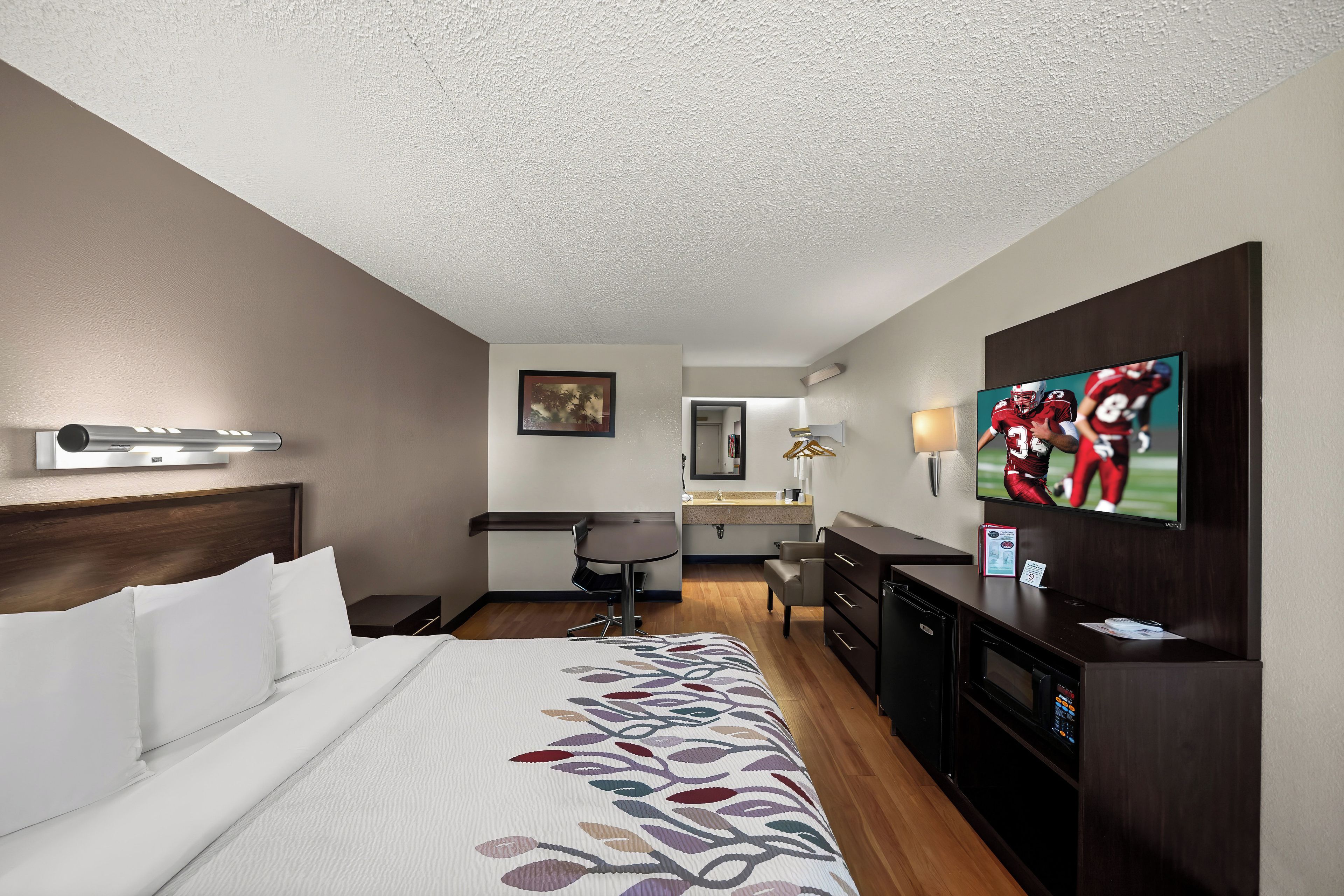 Une chambre d’hôtel avec un lit, un bureau, une chaise, une télévision et une salle de bain à l’arrière-plan.