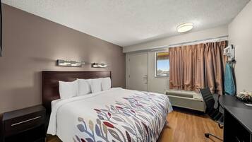Ett hotellrum med en säng, ett skrivbord, en stol, en luftkonditioneringsanläggning och ett fönster med gardiner.