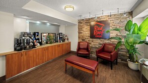 A reception area with a wooden counter, coffee machines, seating, and a wall with a 'Red Roof Inn' sign. - Red Roof Inn Dallas - DFW Airport North (Irving)