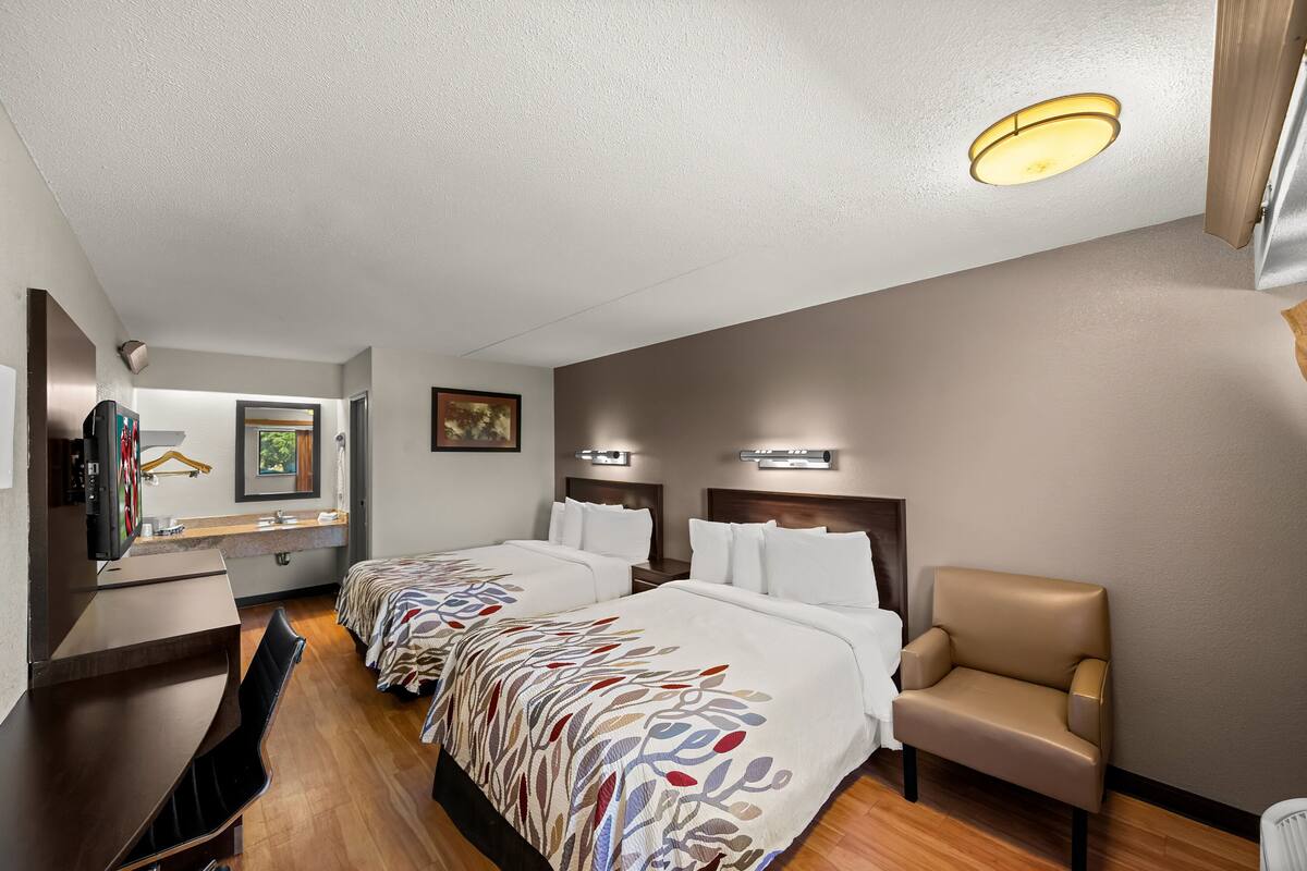 A hotel room with two beds, a desk, a chair, and a TV.