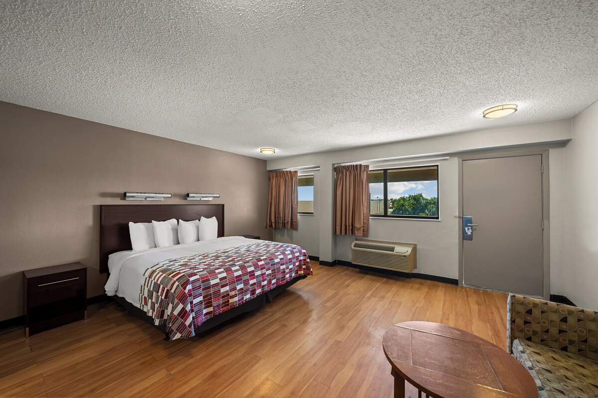 Habitación de hotel con una cama grande, piso de madera, una mesita y una ventana con cortinas.