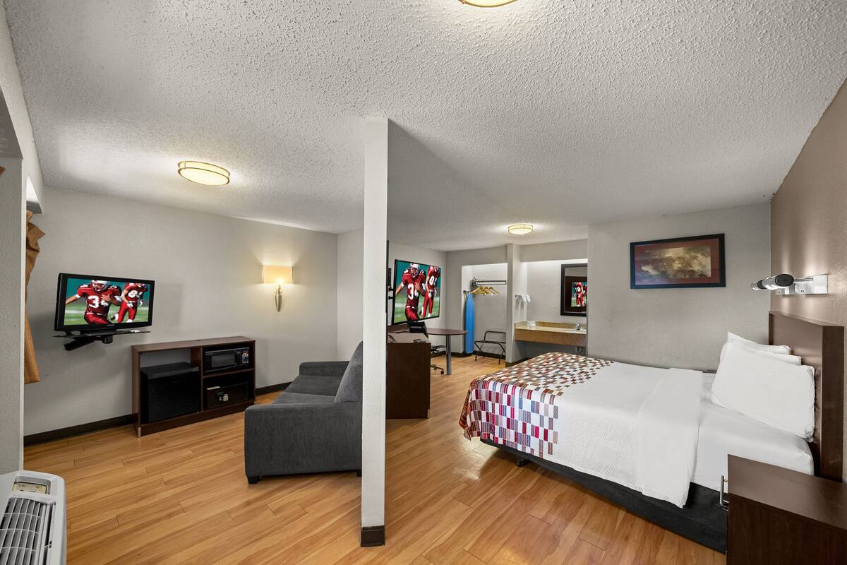 A hotel room with a bed, a desk, a chair, a television, and a wall-mounted TV.