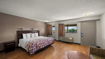 A hotel room with a bed, a small table, a window with curtains, and a door.