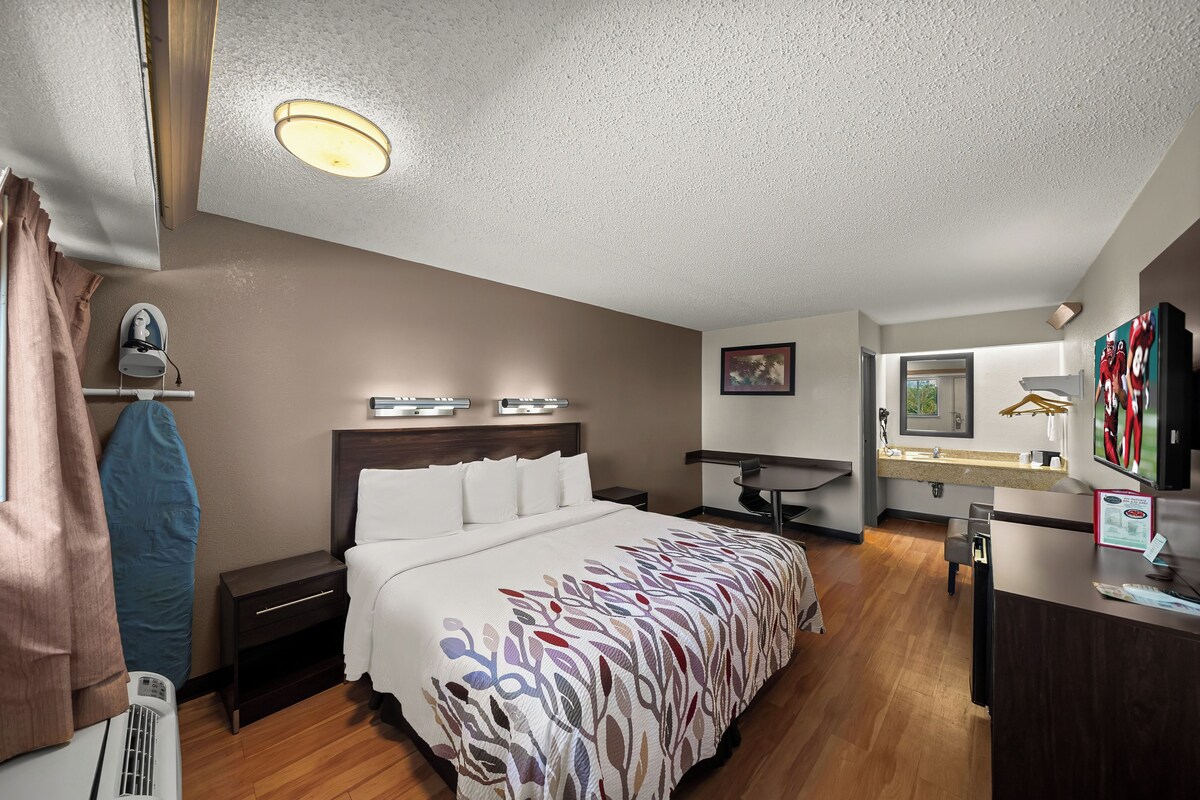 A hotel room with a bed, bedside table, desk, and a television.