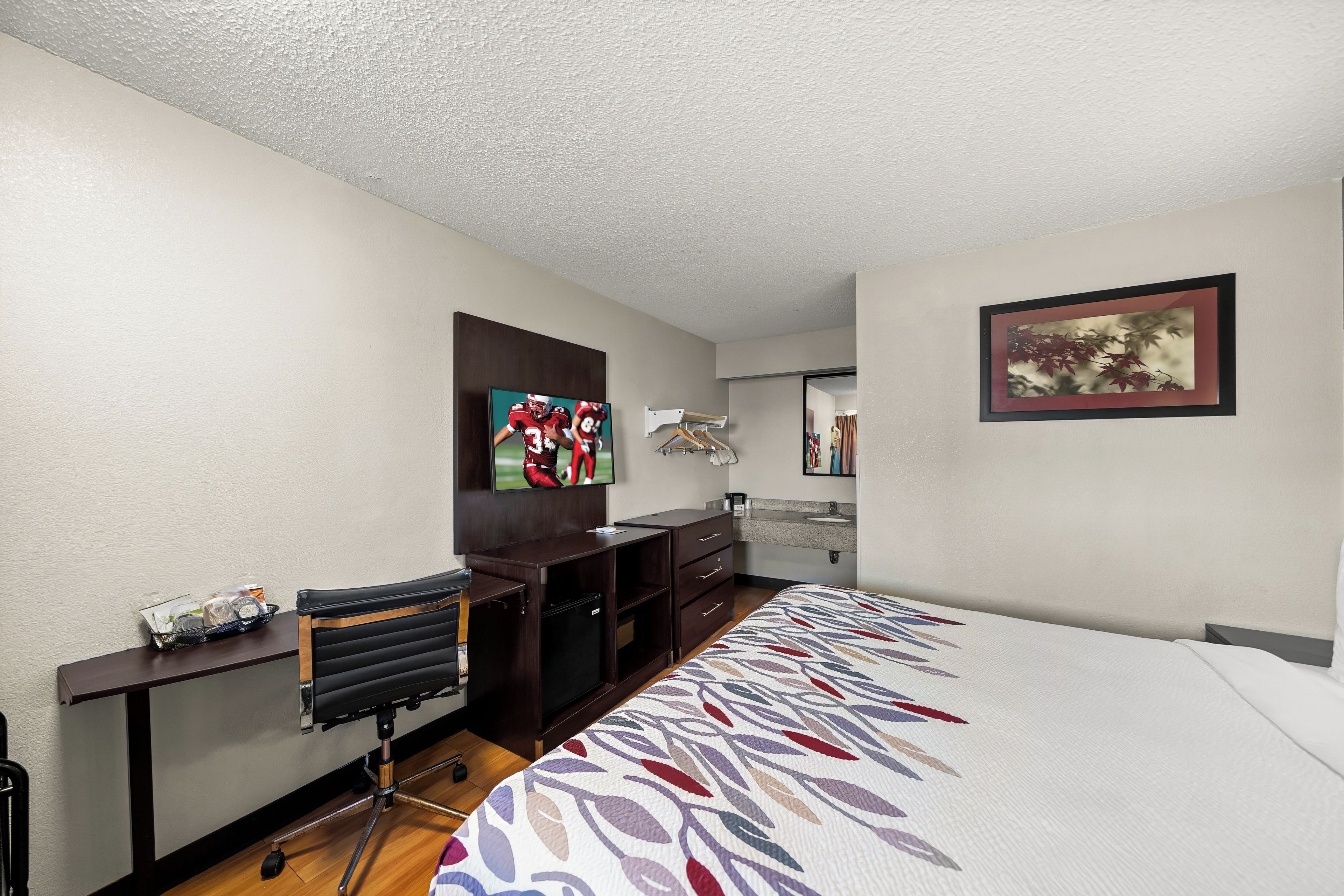 A hotel room with a bed, a desk, a television, a wardrobe, and a bathroom.