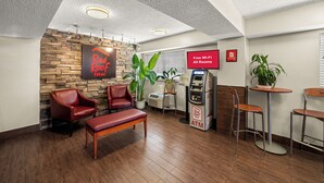 A Red Roof Inn lobby with leather chairs, a wooden bench, an ATM, and a sign indicating free Wi-Fi in all rooms. - Red Roof Inn Dallas - DFW Airport North (Irving)