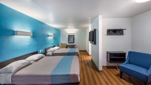 A hotel room with two beds, a blue armchair, a TV, and a small table. - Motel 6 Irving, TX - Irving DFW Airport East (Irving)