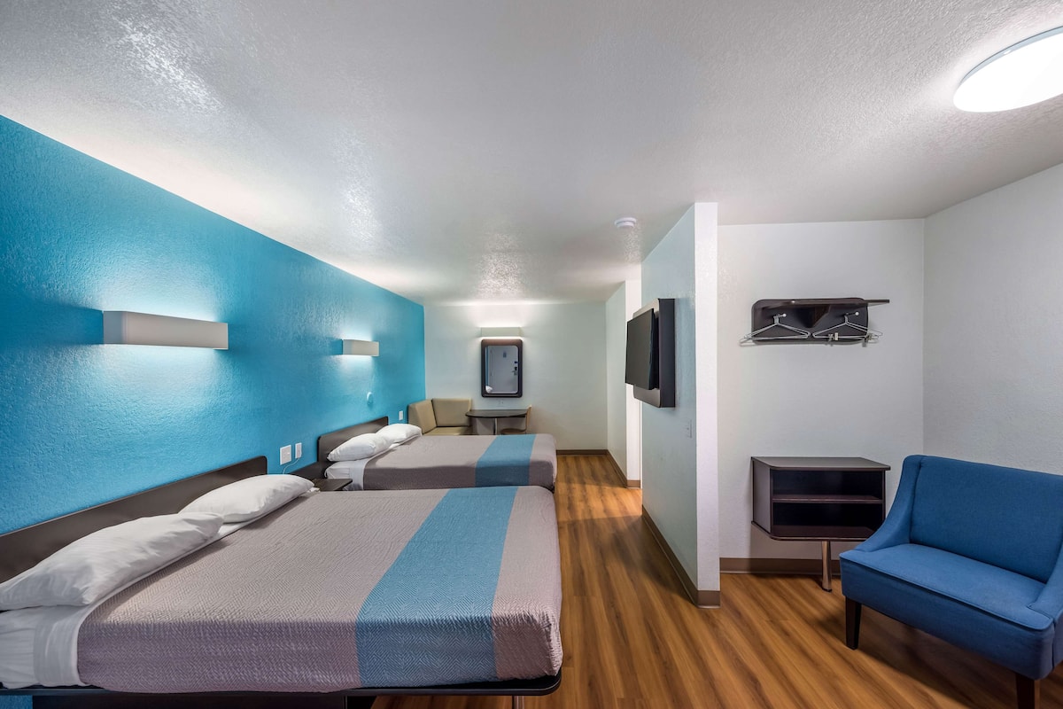 Una habitación de hotel con dos camas, un sillón azul, un televisor y una mesita.