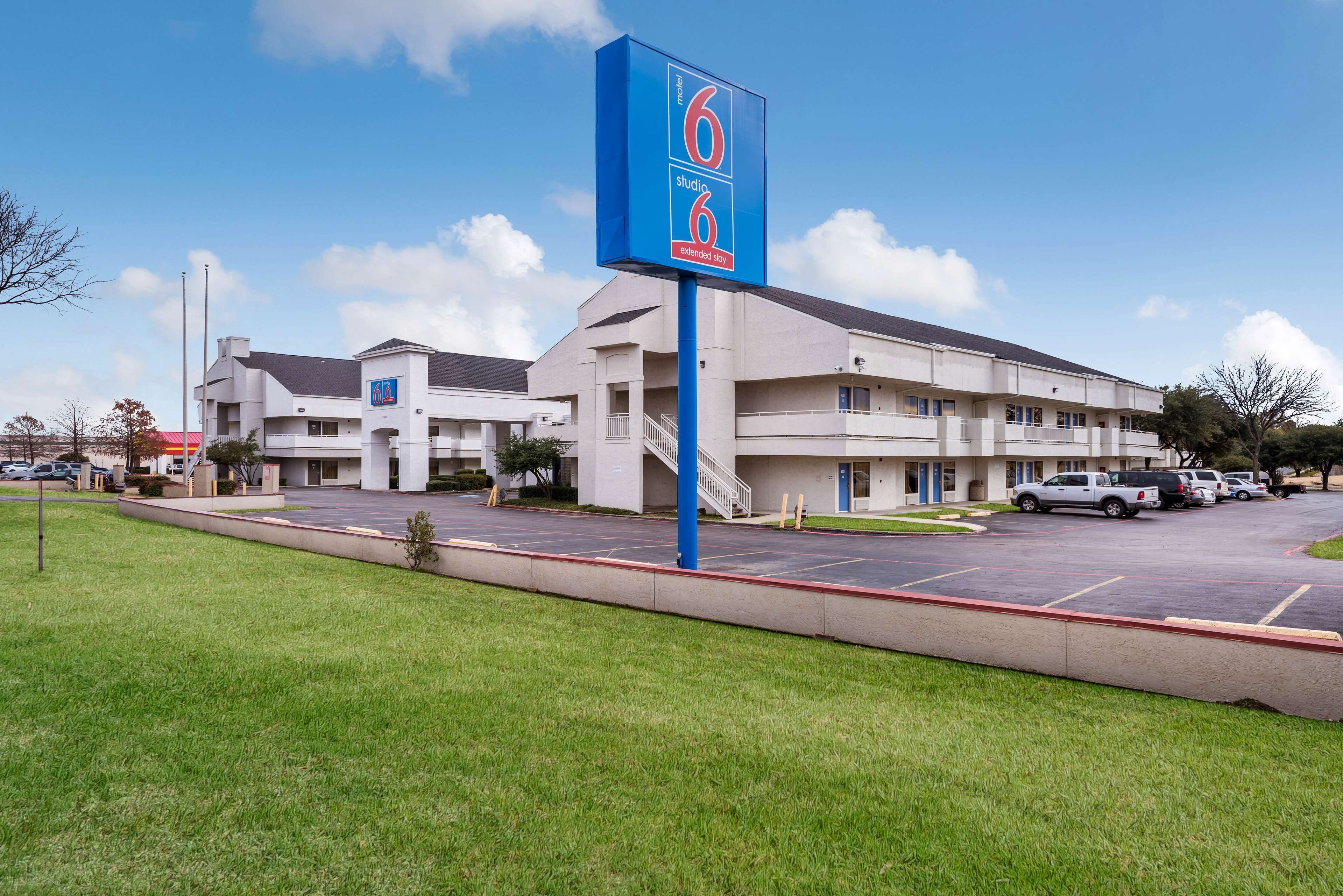 Un motel con un letrero azul, varios espacios de estacionamiento y un área verde al frente.