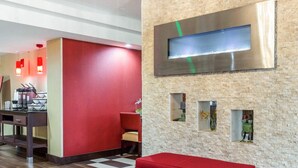 A lobby with a red bench, a kitchen area with a stove, and a wall with a large mirror and small windows. - Comfort Inn Conyers (Conyers)