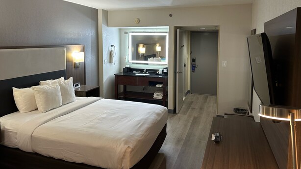 A hotel room with a large bed, a vanity with a mirror, a television, and a door leading to another room. - Comfort Inn Conyers (Conyers)